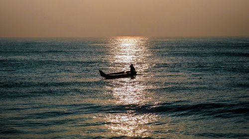 Silhouette man in sea against sky during sunset