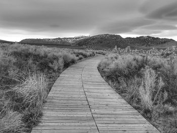 Boardwalk leading towards landscape against sky