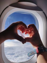 Low angle view of hand against sky seen through airplane