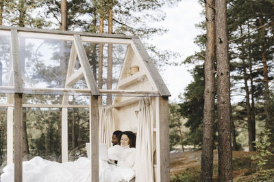 Woman using laptop while working remotely by man in cottage