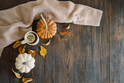 Flat lay of pumpkins, dried leaves, accessories and tea with lemon in cup on wooden background.