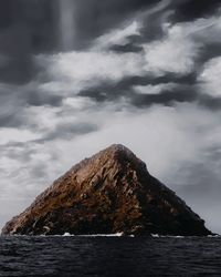 Rock formation in sea against cloudy sky