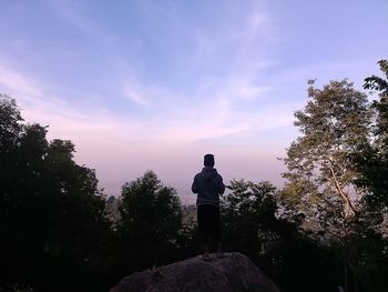 Rear view of man standing on rock against sky