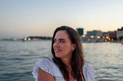 Portrait of pretty girl sitting on waterfront in city by sea during evening hours