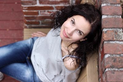 Portrait of smiling young woman sitting on brick wall