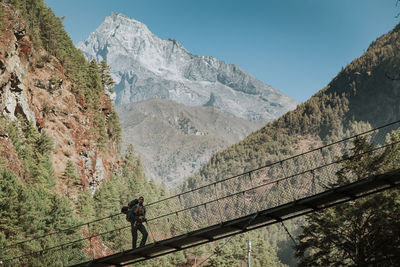 People walking on footbridge against mountains