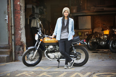 Portrait of female standing with bike outside auto repair shop