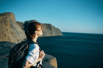 Man standing on rock looking at sea against clear sky