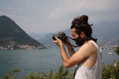 Man photographing through camera by lake against sky