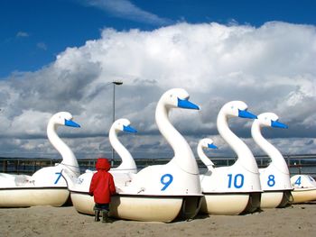 Rear view of child standing by swan shape pedal boats at beach