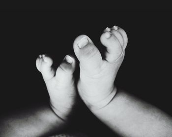 Low section of baby feet with hand on black background