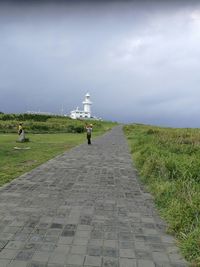 Rear view of people walking on footpath leading towards field against sky