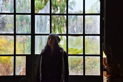 Thoughtful woman looking up while standing against window