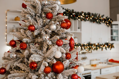 Closeup of  decorated christmas tree with red and silver balls on blurred sparkling festive kitchen.