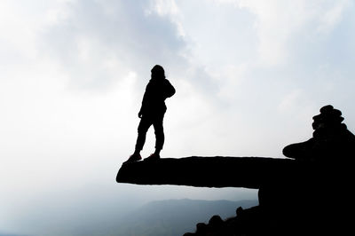Low angle view of silhouette woman standing on rock against sky in foggy weather