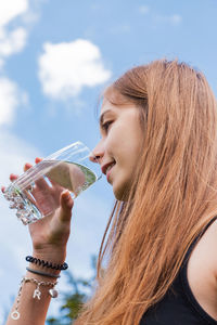 Woman drinking water in glass against sky