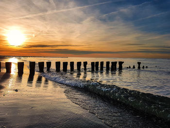 Wooden posts on beach against sky during sunset