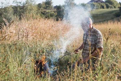 Man holding stick over campfire on grassy field