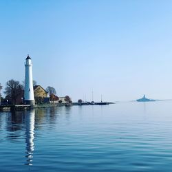 Lighthouse by sea against clear sky