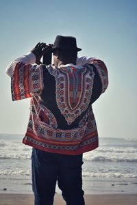 Rear view of man standing at beach against sky