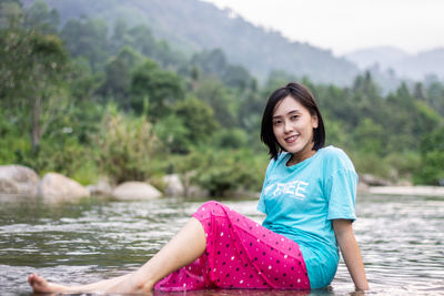 Portrait of smiling young woman sitting against mountain