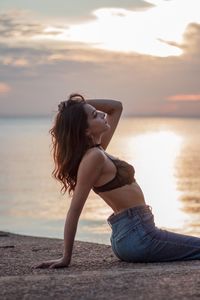 Full length of young woman on beach against sky during sunset