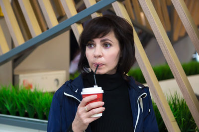 Adult brunette drinks coffee in cafe with interest looking around.