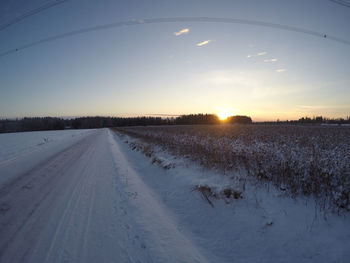 Snow covered land against sky during sunset