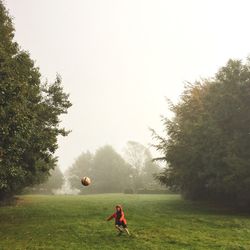 Full length of boy playing with ball on field during foggy weather