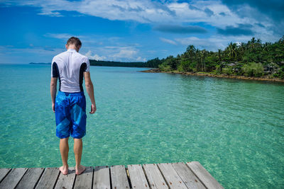 Rear view of man standing on pier over sea against sky