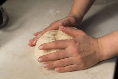 Cropped hands kneading dough on table