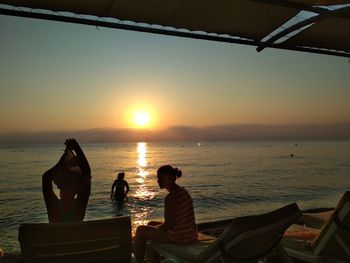 People at beach against sky during sunset