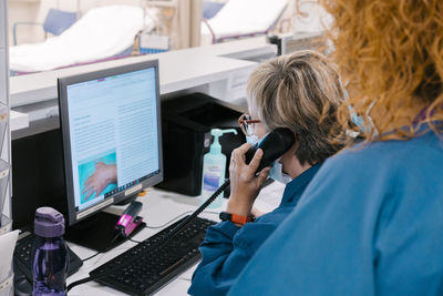 Nurse with colleague talking on telephone and using computer at hospital