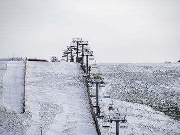 Electricity pylon on snow covered landscape against sky