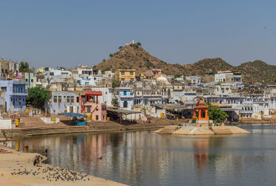 Buildings by lake in city against clear sky