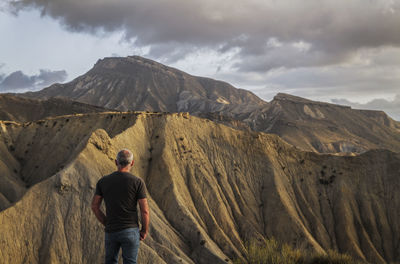 Rear view of man walking on mountain against sky, in tabernas desert, almeria, spain