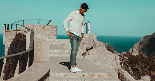 Man standing on staircase by sea against sky