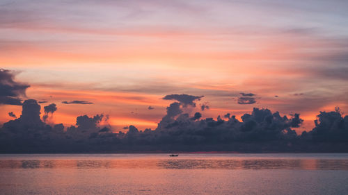 Island's bay dawn with orange sky and lonely boat against dramatic cloud. koh samui, thailand.