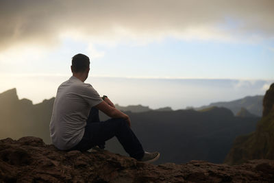 Full length of man sitting on rock against sky