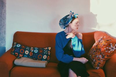 Woman wearing headscarf while sitting on couch at home