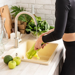 Midsection of woman washing vegetables in sink