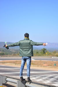 Rear view of man standing on railing against blue sky