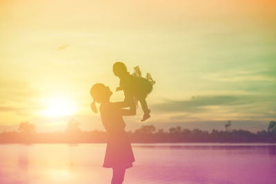 Woman standing by lake against sky during sunset