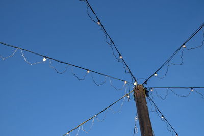 Low angle view of illuminated string light against clear blue sky