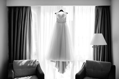 Front view of wedding dress hanging against curtain