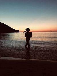 Silhouette woman standing on beach against sky during sunset