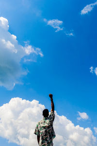 Rear view of man standing against blue sky
