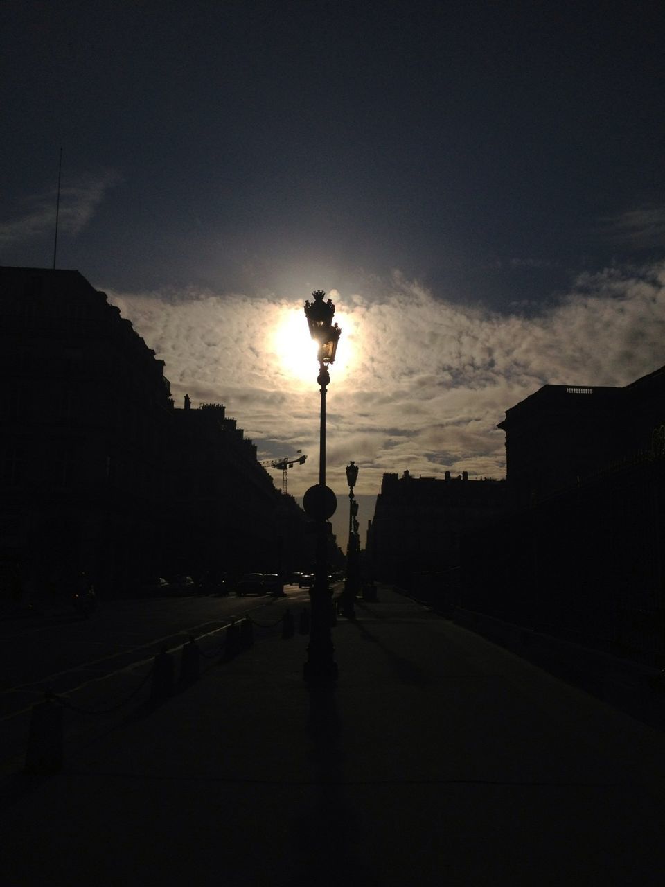 street light, sky, street, building exterior, road, the way forward, transportation, silhouette, built structure, car, architecture, sunlight, sun, sunset, land vehicle, cloud - sky, lighting equipment, tree, sunbeam, outdoors