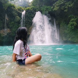 Side view of woman sitting by waterfall