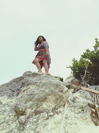 Low angle view of woman standing on rock against clear sky